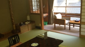 A traditional Japanese-style room with tatami flooring, a low table with a placemat, a cushioned bench, and a sliding door leading to a balcony. - Sento Ryokan (Toyooka)