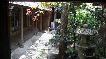 A traditional Japanese garden with stone pathways, a stone lantern, and a wooden building with sliding doors.