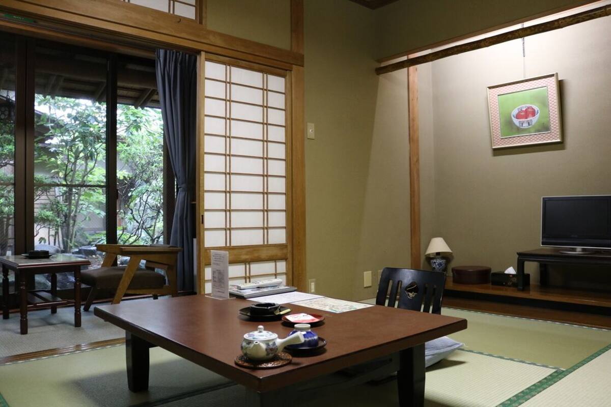 A traditional Japanese room with tatami flooring, a low table with a tea set, a television, and a framed picture on the wall.