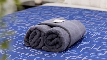 A neatly made bed with a blue patterned bedspread and a rolled gray towel on top.