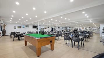 A spacious indoor area with a pool table, multiple dining tables, and chairs.