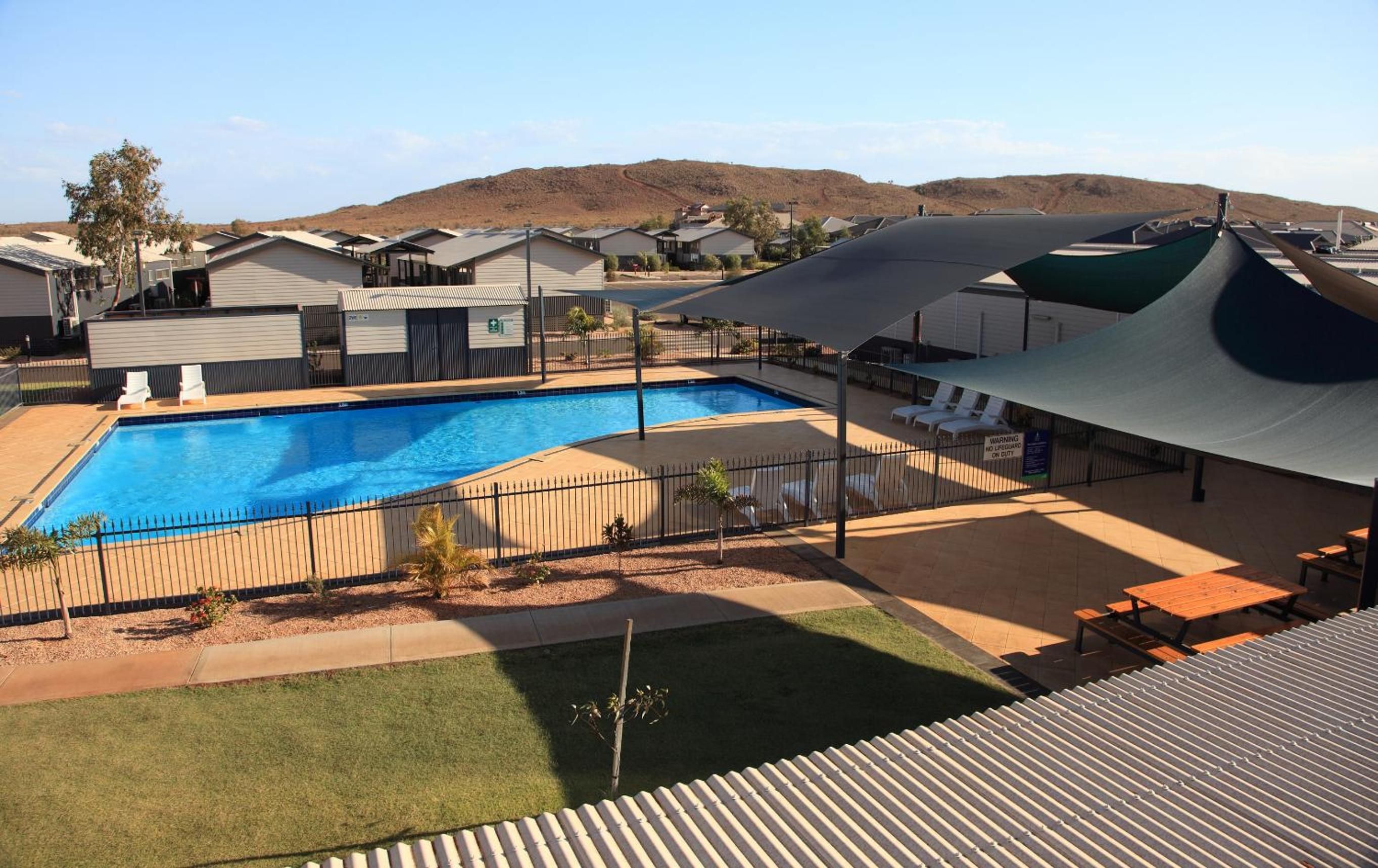Ein Pool, umgeben von einer eingezäunten Liegefläche mit Liegestühlen und einem schattigen Picknicktisch.
