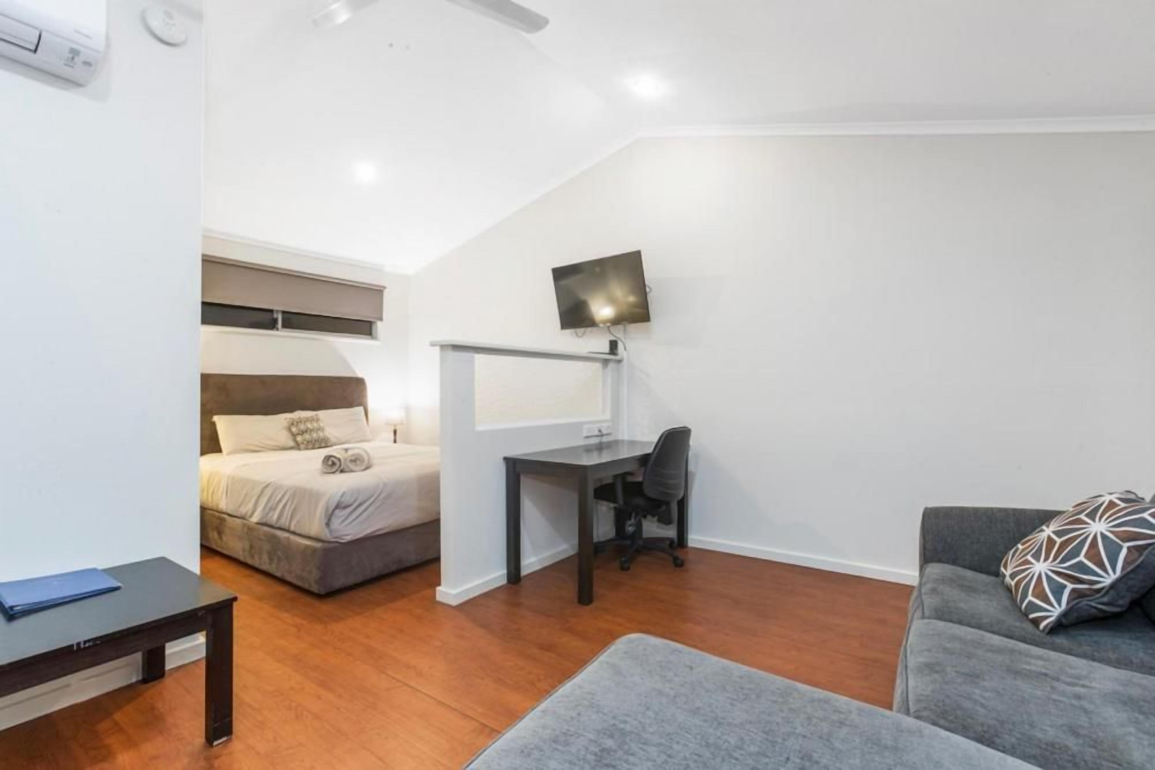 Habitación compacta con cama, escritorio, silla, sofá y televisor de pantalla plana montado en la pared.