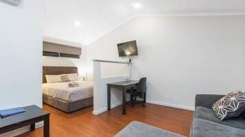 Habitación compacta con cama, escritorio, silla, sofá y televisor de pantalla plana montado en la pared.