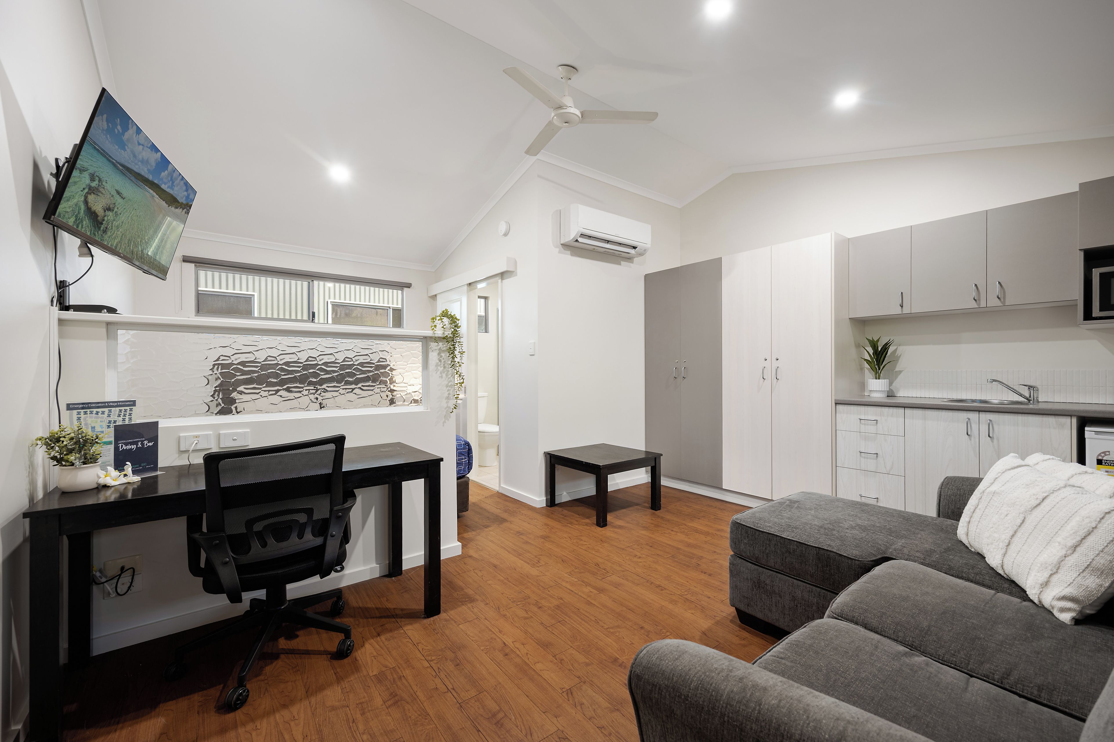 A modern living space with a dining area, kitchenette, and a grey sofa.