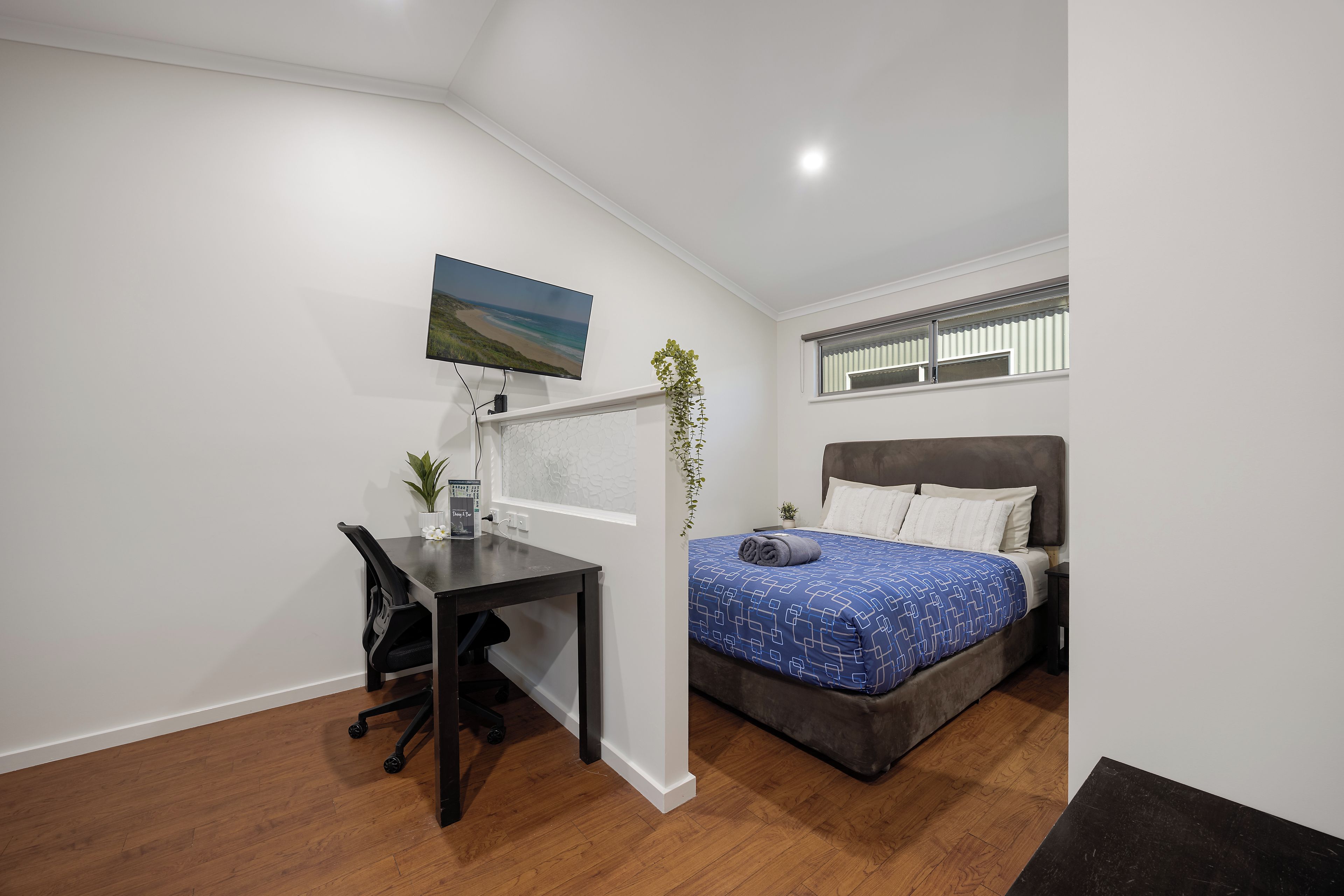 A bedroom with a bed, a desk, a chair, a television, and a window.