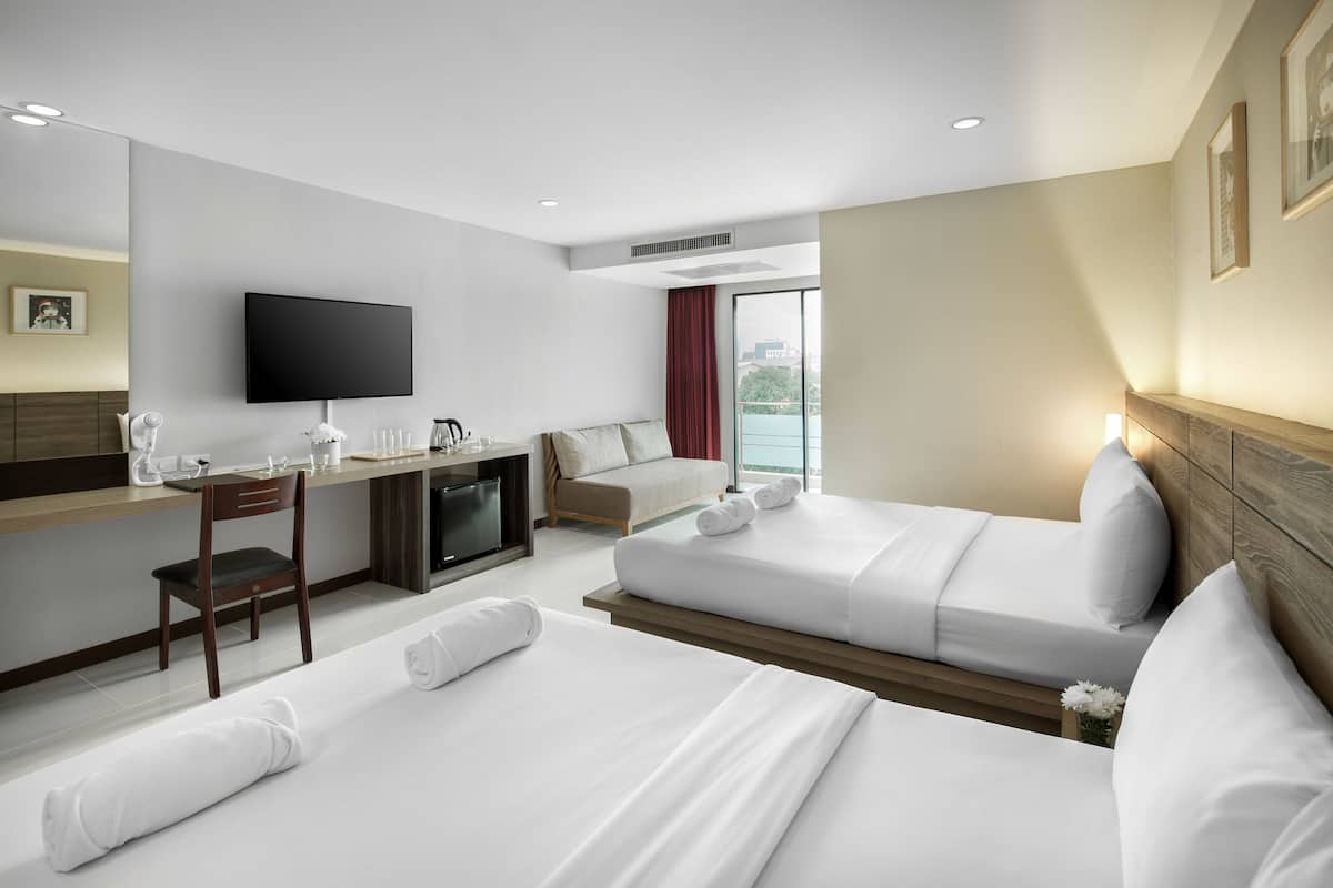 A hotel room with two beds, a desk, a TV, and a view of the city.