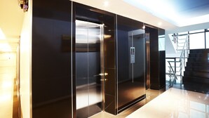 Un ascensor moderno con puertas de cristal, barandilla de metal y panel de control.