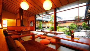 A traditional Japanese-style interior with tatami flooring, wooden furniture, and large windows offering a view of a garden and traditional buildings. - Onishiya Suishoen (Toyooka)