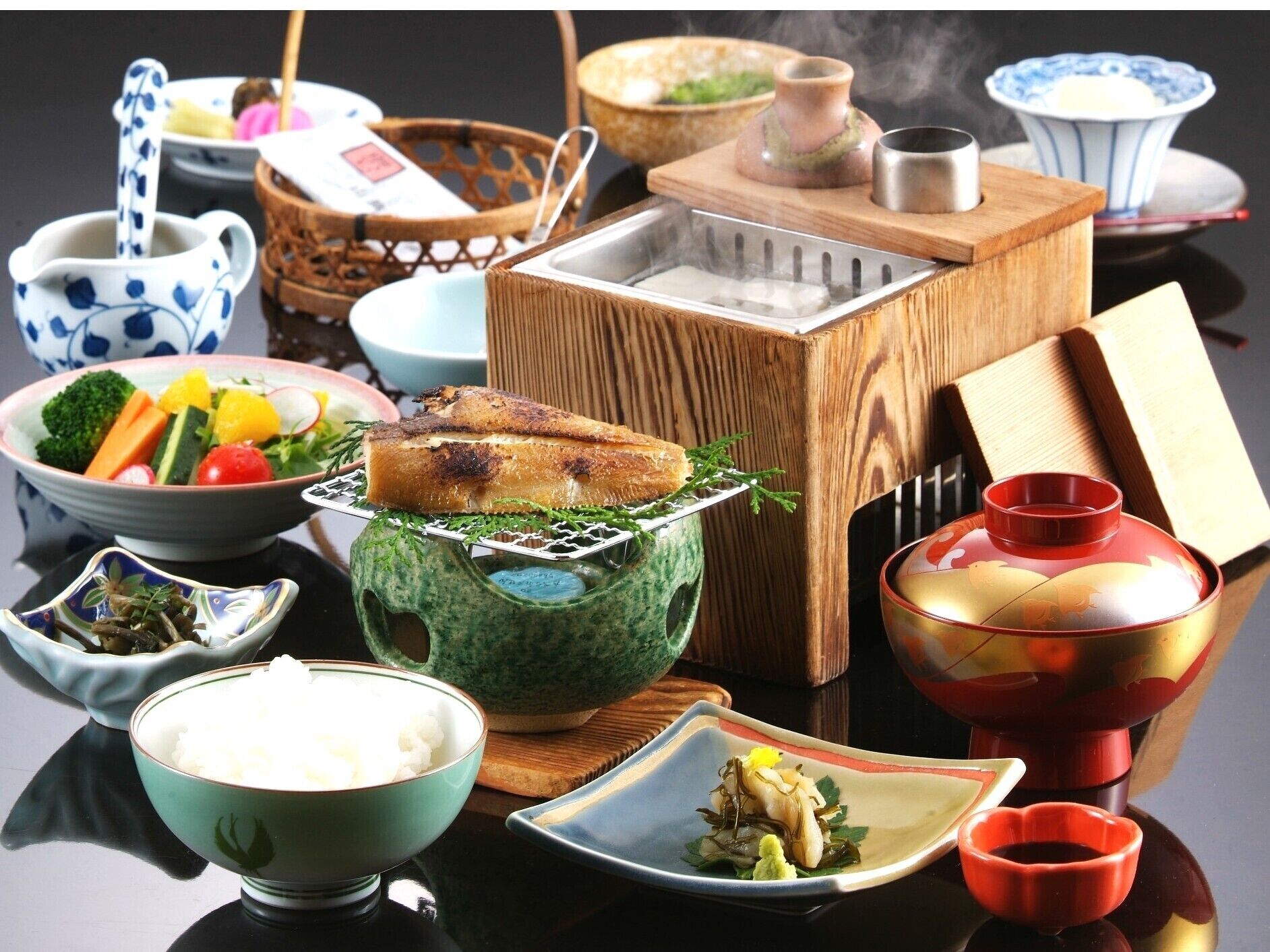 A traditional Japanese meal setup with various dishes, including rice, vegetables, and fish, served on a black table.