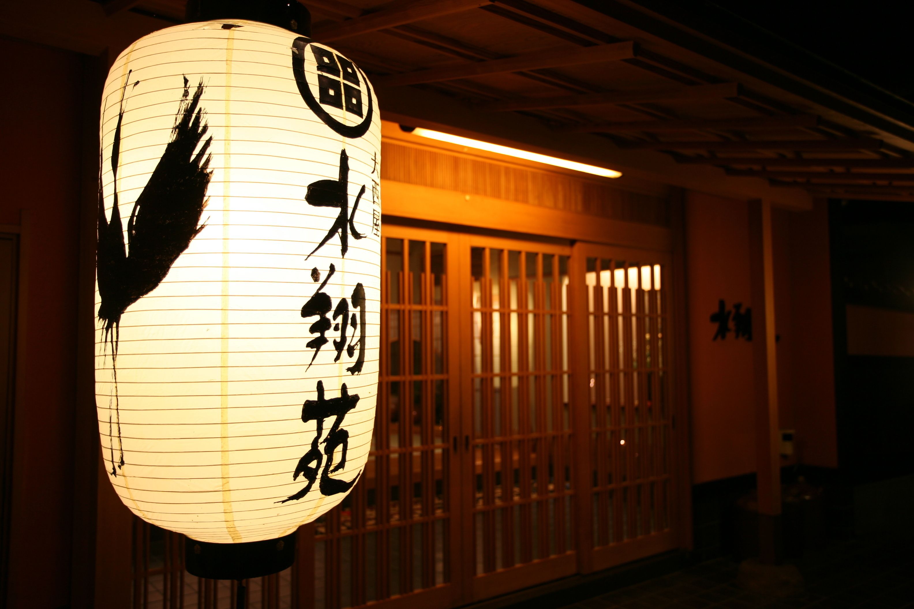 A traditional Japanese lantern with calligraphy, a wooden sliding door, and a sign with Japanese characters.
