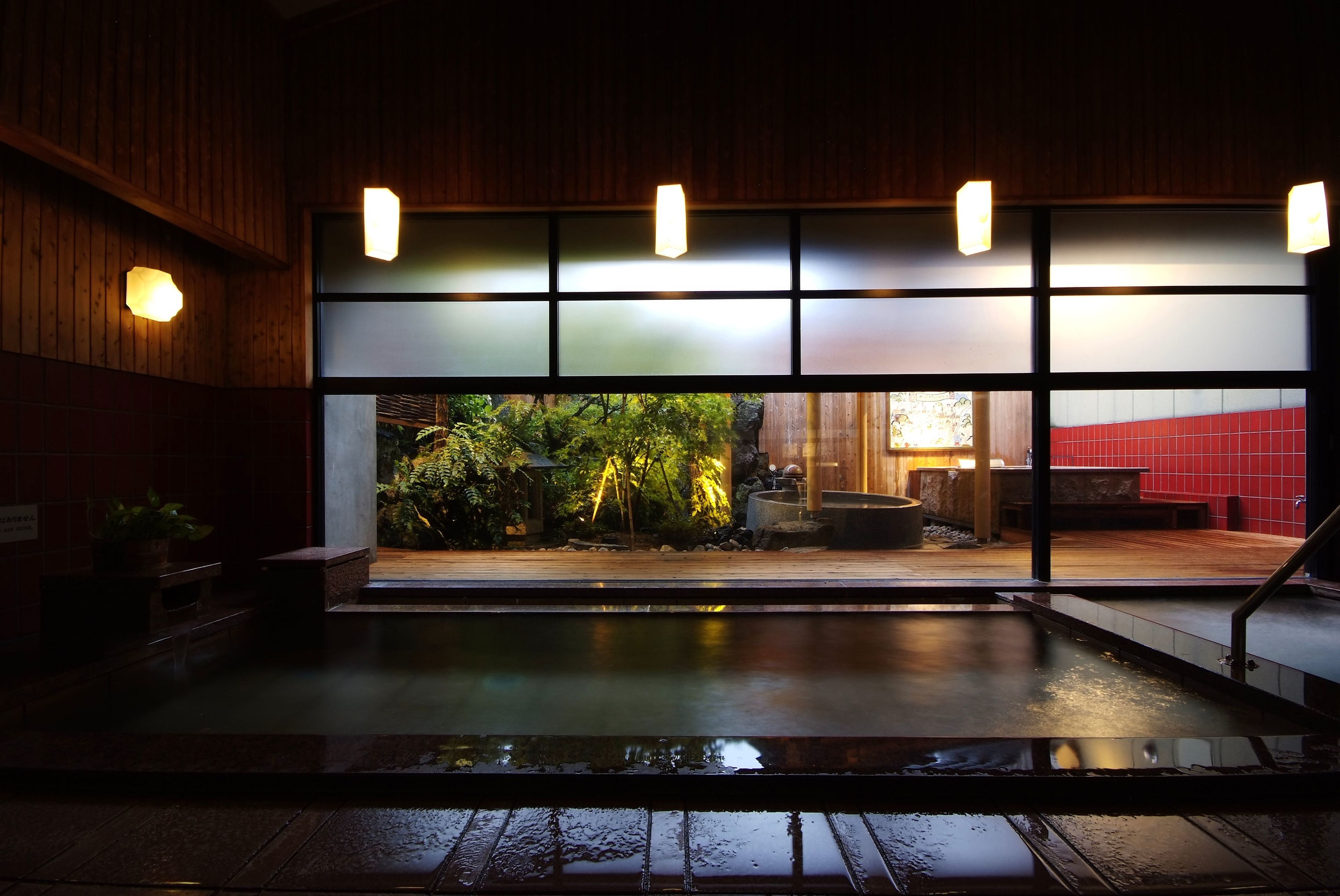 Ein traditionelles japanisches Onsen mit Holzinnenraum, Blick auf einen Garten und einer roten Ziegelfassade.