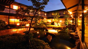 A traditional Japanese-style building with a koi pond and well-lit garden at dusk. - Onishiya Suishoen (Toyooka)