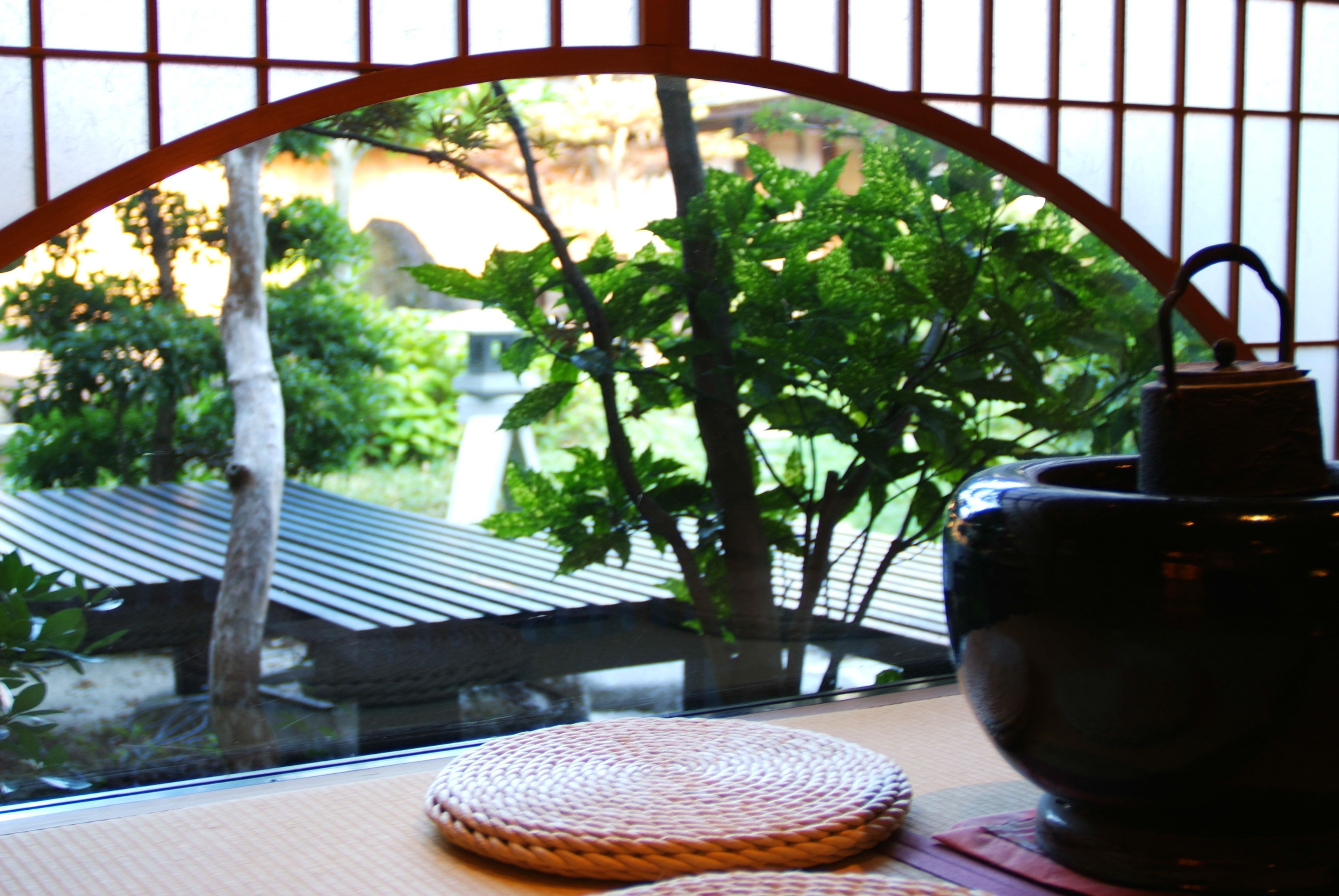 A view through a window with a woven mat on the sill, a dark ceramic pot, and a metal gate.