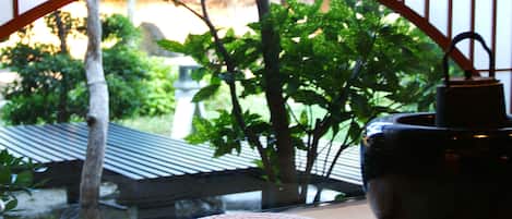 A view through a window with a woven mat on the sill, a dark ceramic pot, and a metal gate.