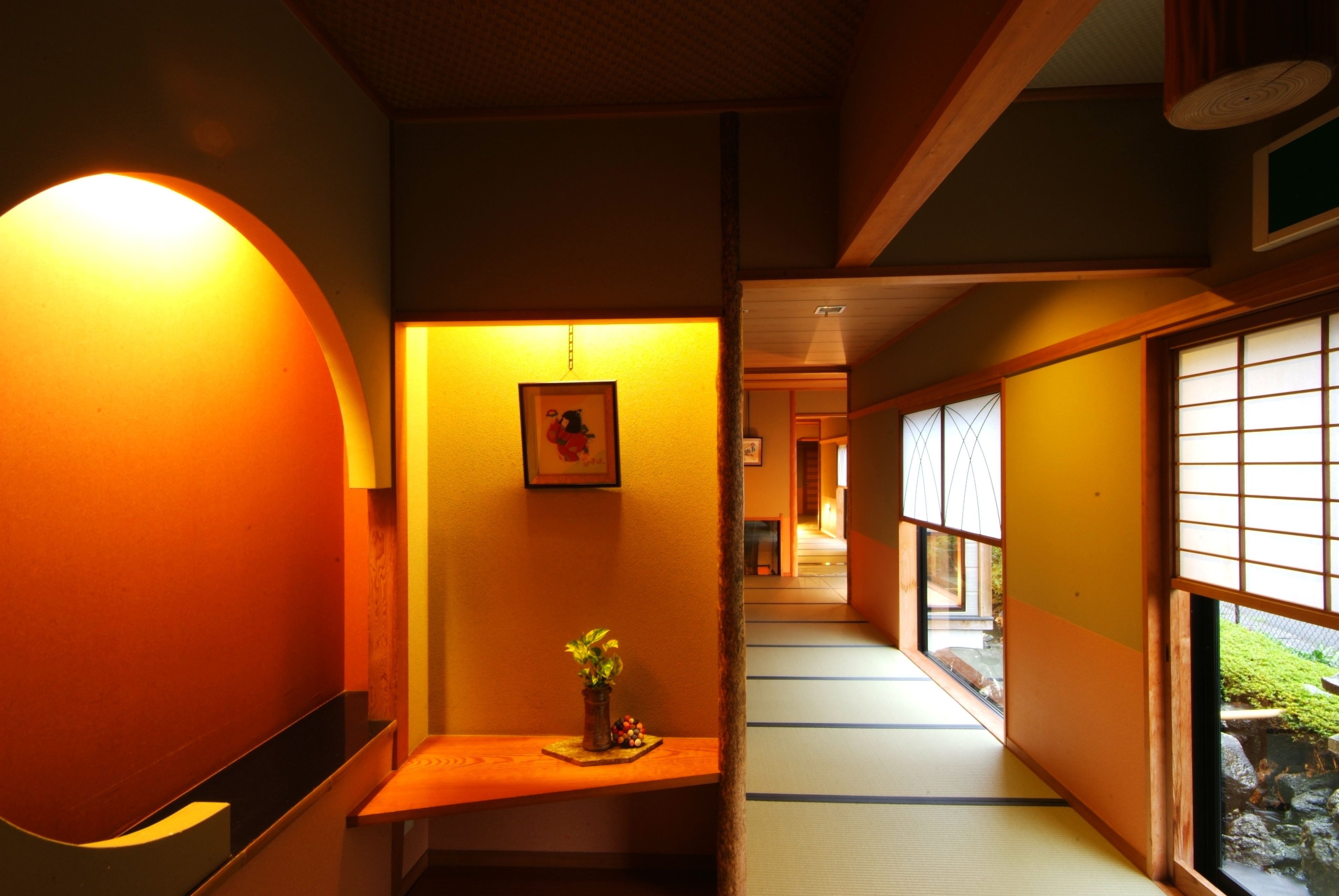 A traditional Japanese interior with tatami flooring, a wooden bench, a wall-mounted picture, and a sliding door leading to another room.