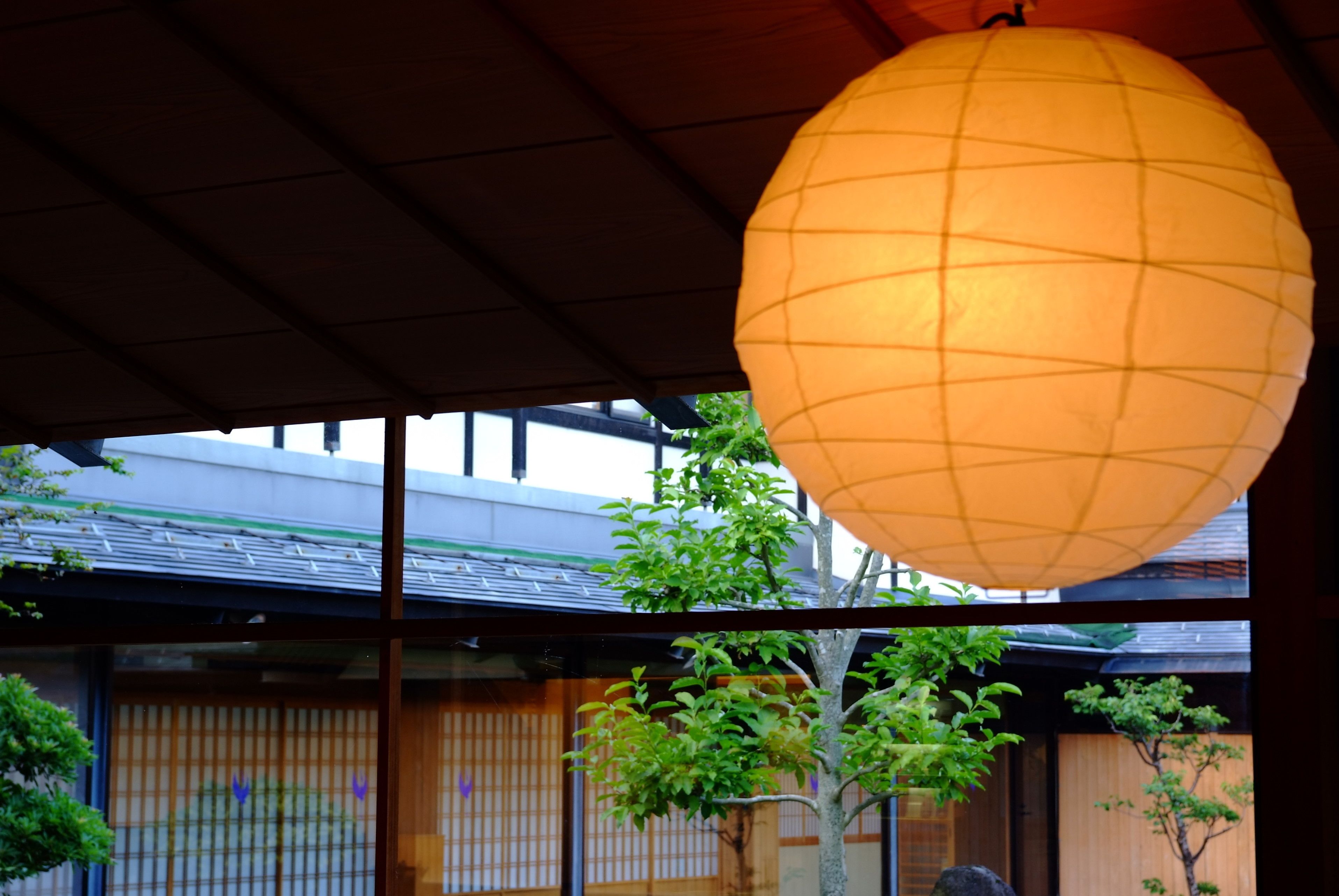 A traditional Japanese building with a large hanging paper lantern, wooden shoji screens, and a view of the surrounding greenery.