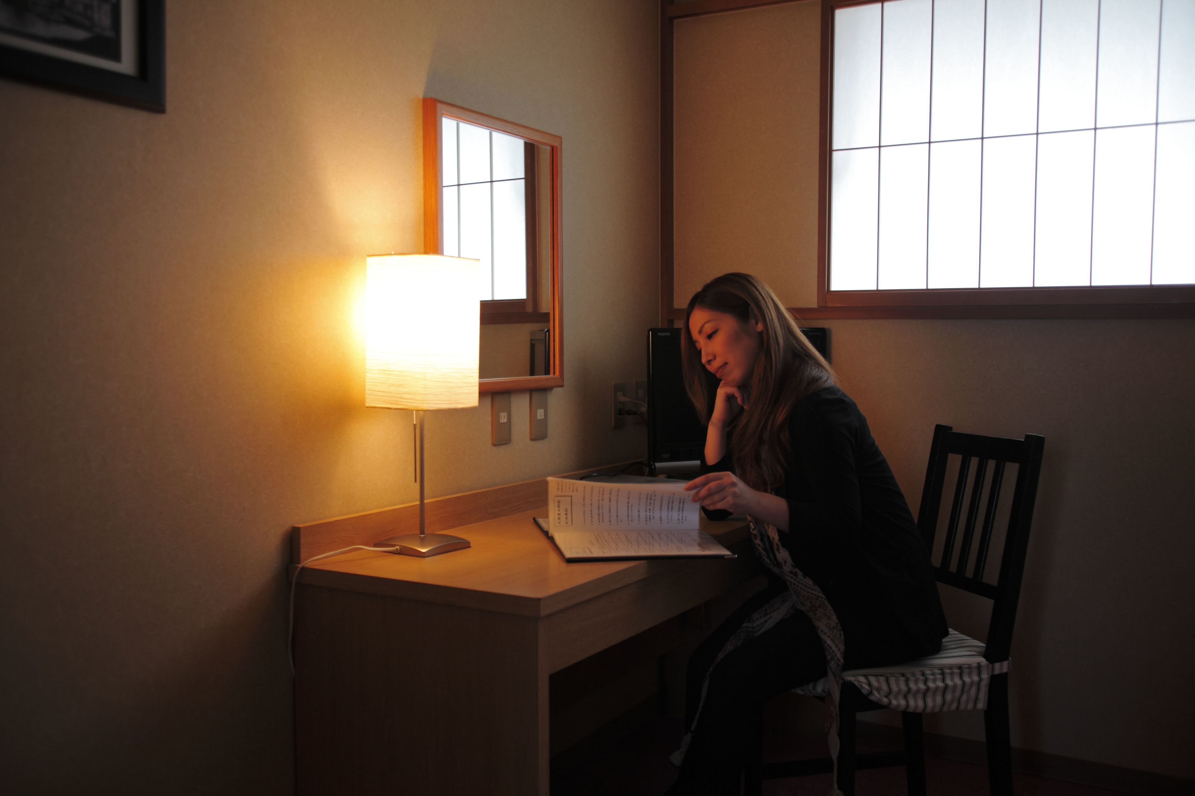A person sitting at a desk with a lamp, a chair, and a window.