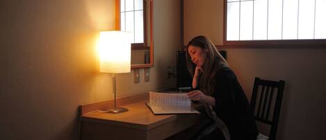 A person sitting at a desk with a lamp, a chair, and a window.