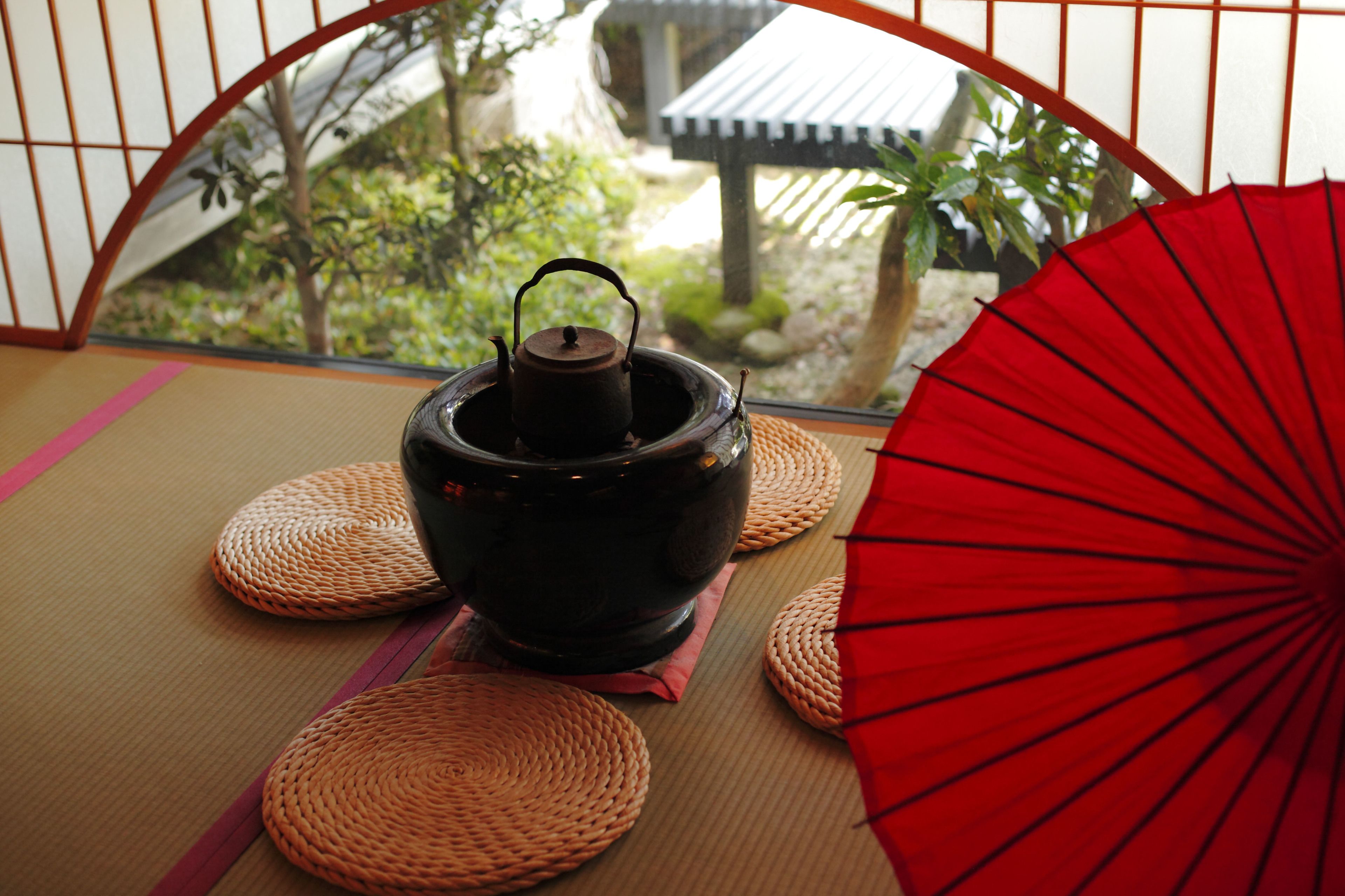 A traditional Japanese tea ceremony setup with a black tea pot, woven mats, and a red fan.