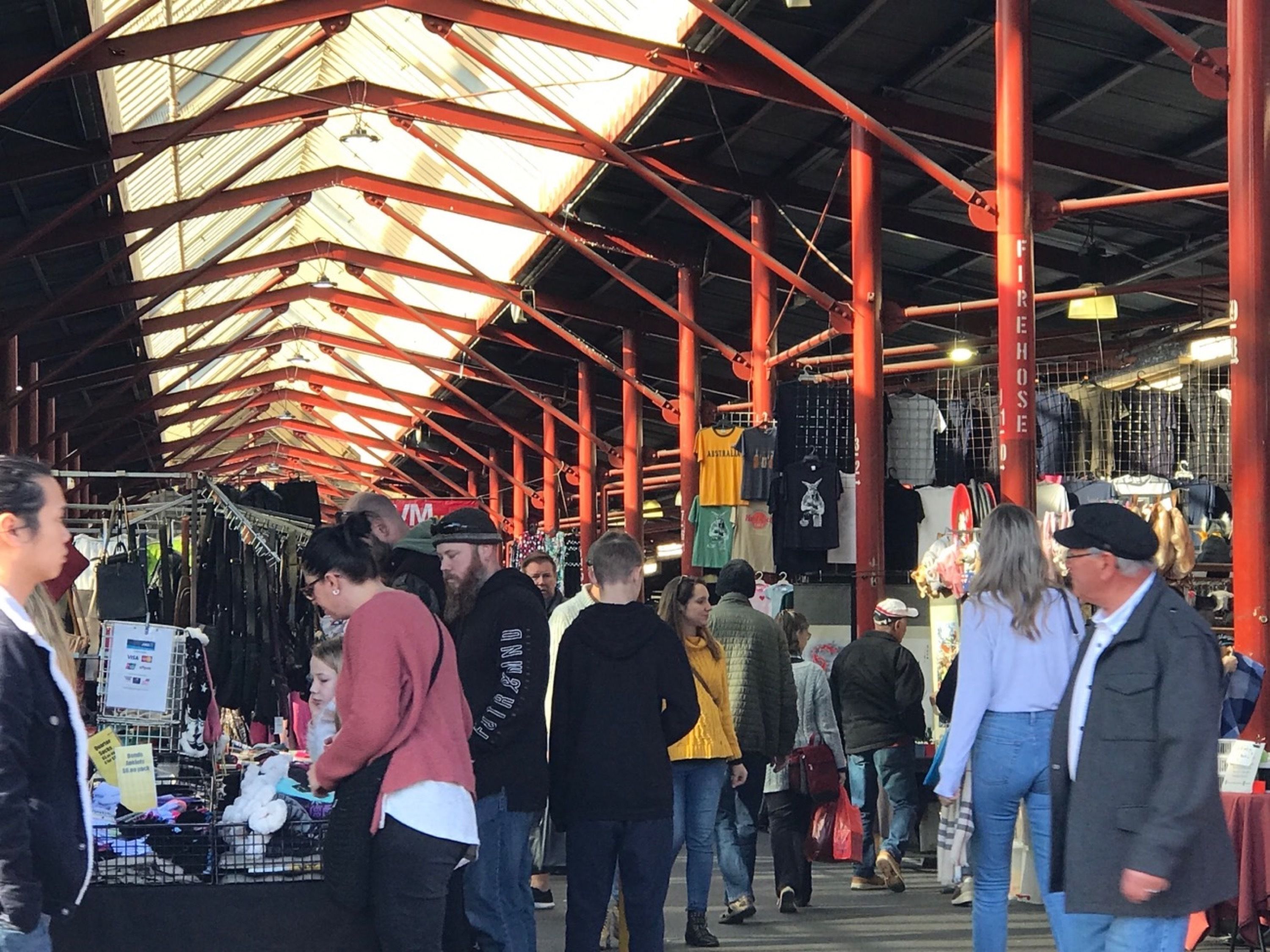 Een overdekte markt met rode dragers en verschillende kraampjes die spullen verkopen.