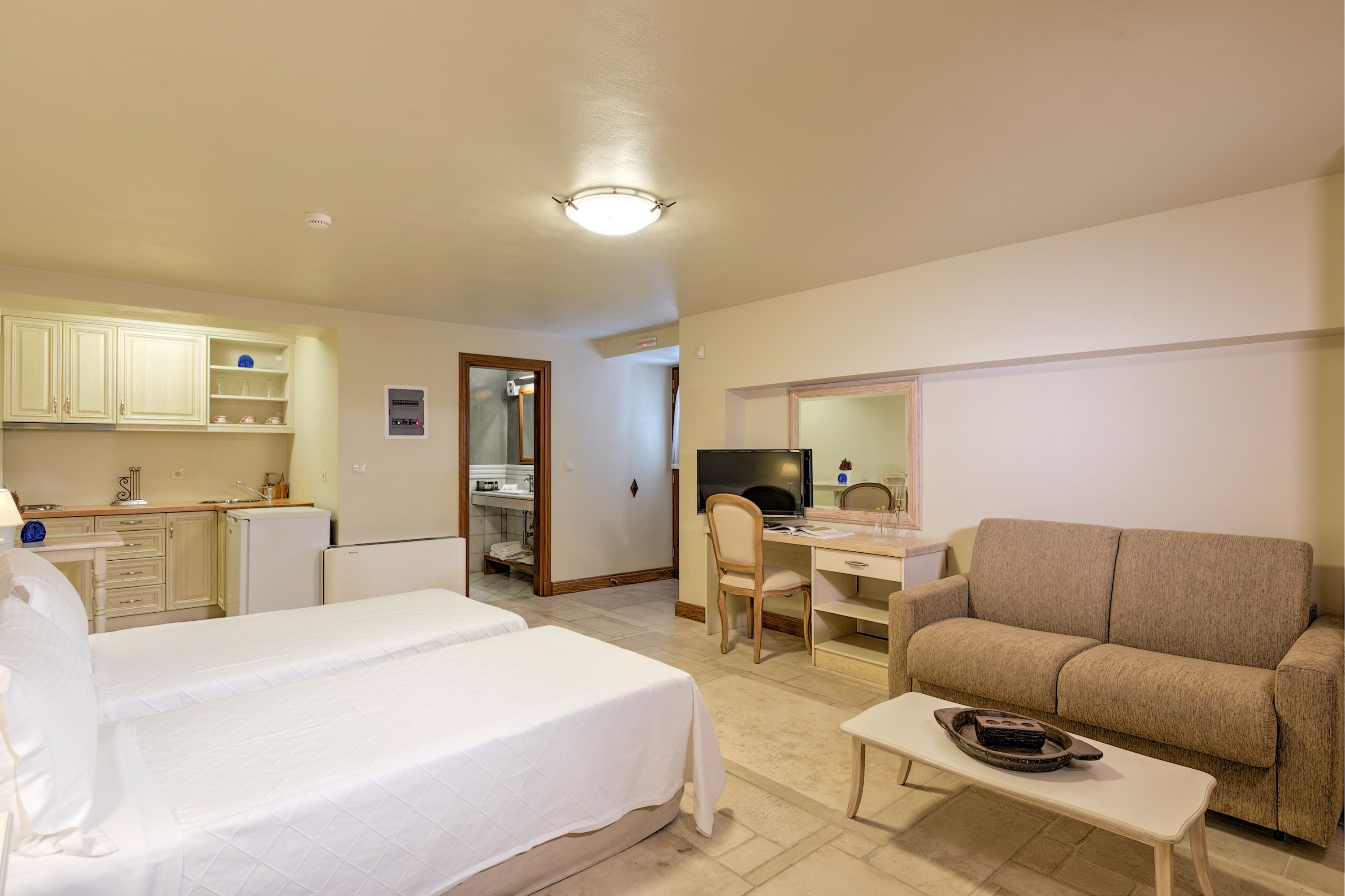 A hotel room with two beds, a desk, a sofa, and a small kitchenette.