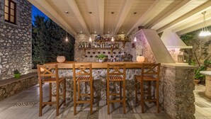 Eine Außenbar mit Steinmauern, Holzstühlen und einer Auswahl an Flaschen und Gläsern.