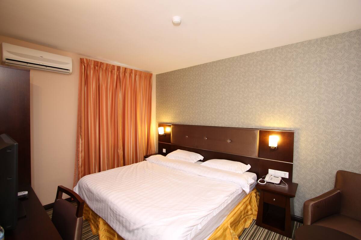 Ein Hotelzimmer mit einem großen Bett, einem Schreibtisch mit Stuhl, einem Fernseher, einer Klimaanlage und einem Telefon.