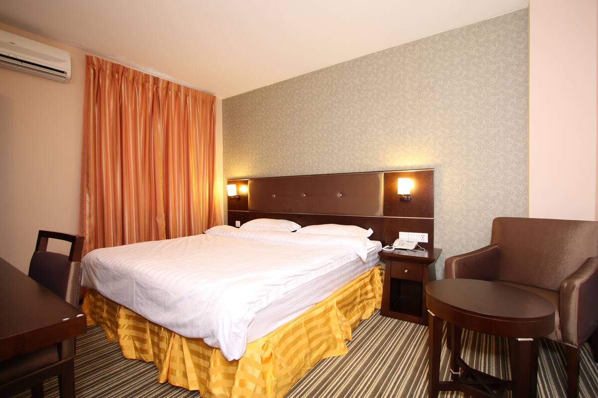 Ein Hotelzimmer mit einem großen Bett, einem Schreibtisch, einem Sessel und einem Nachttischchen mit Telefon.
