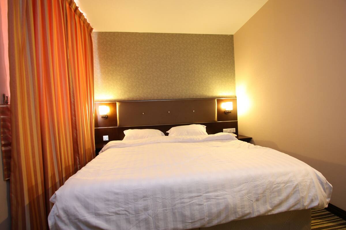Ein Hotelzimmer mit einem großen Bett, zwei Nachttischlampen und einem Kopfteil.