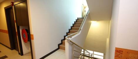 A staircase with a handrail, a door with a red handle, and a patterned wall.