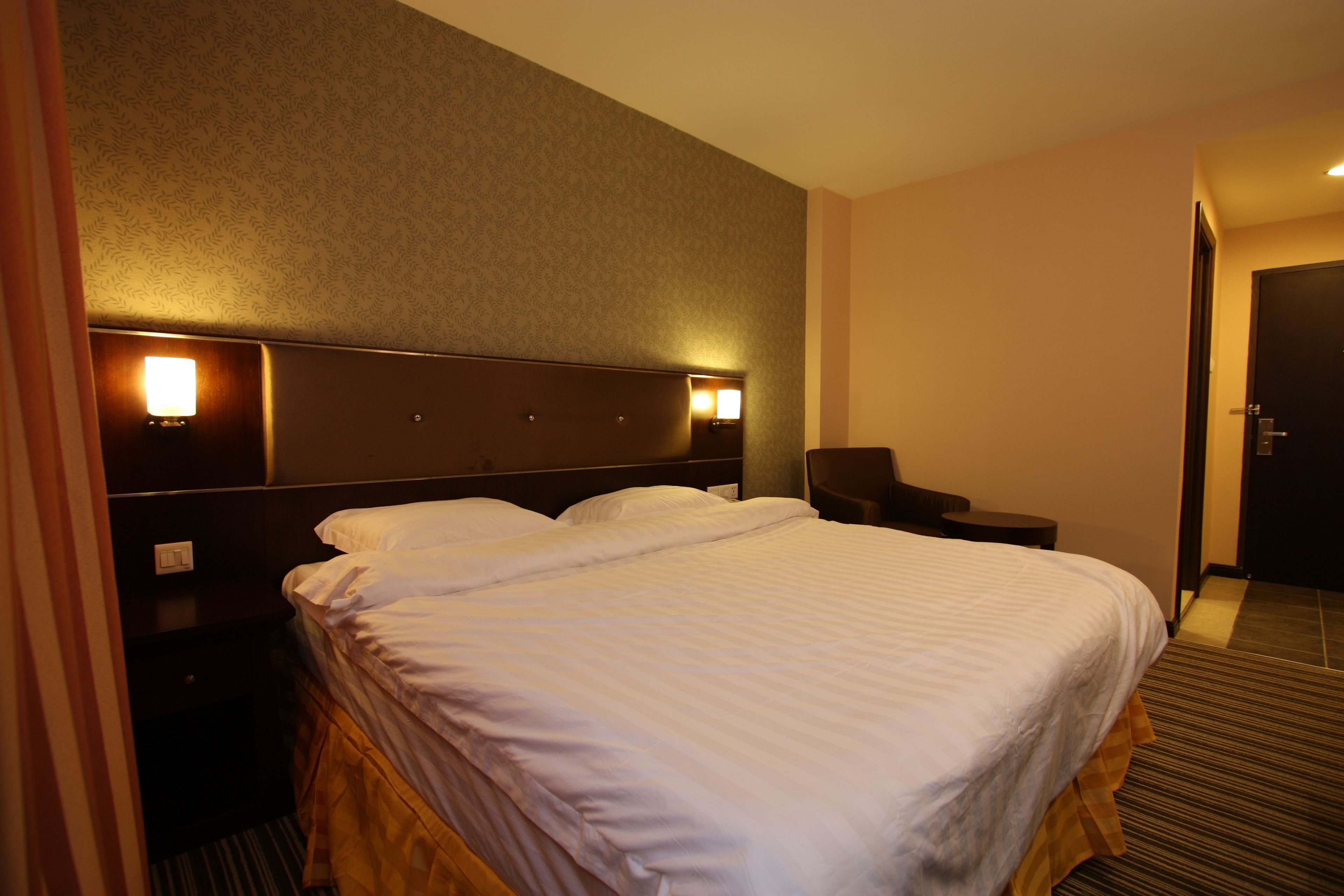 A hotel room with a large bed, two bedside tables with lamps, a chair, and a door.