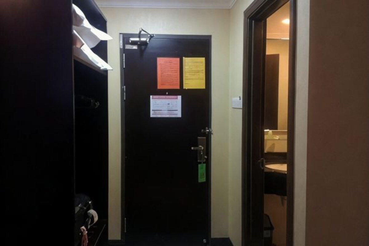 A hotel room entrance with a closed door, a visible bathroom, and a small desk with a chair.
