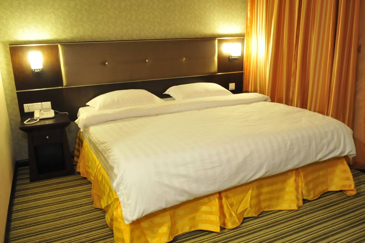 Ein Hotelzimmer mit einem großen Bett, einem Nachttisch, einer Lampe und einem Vorhang.
