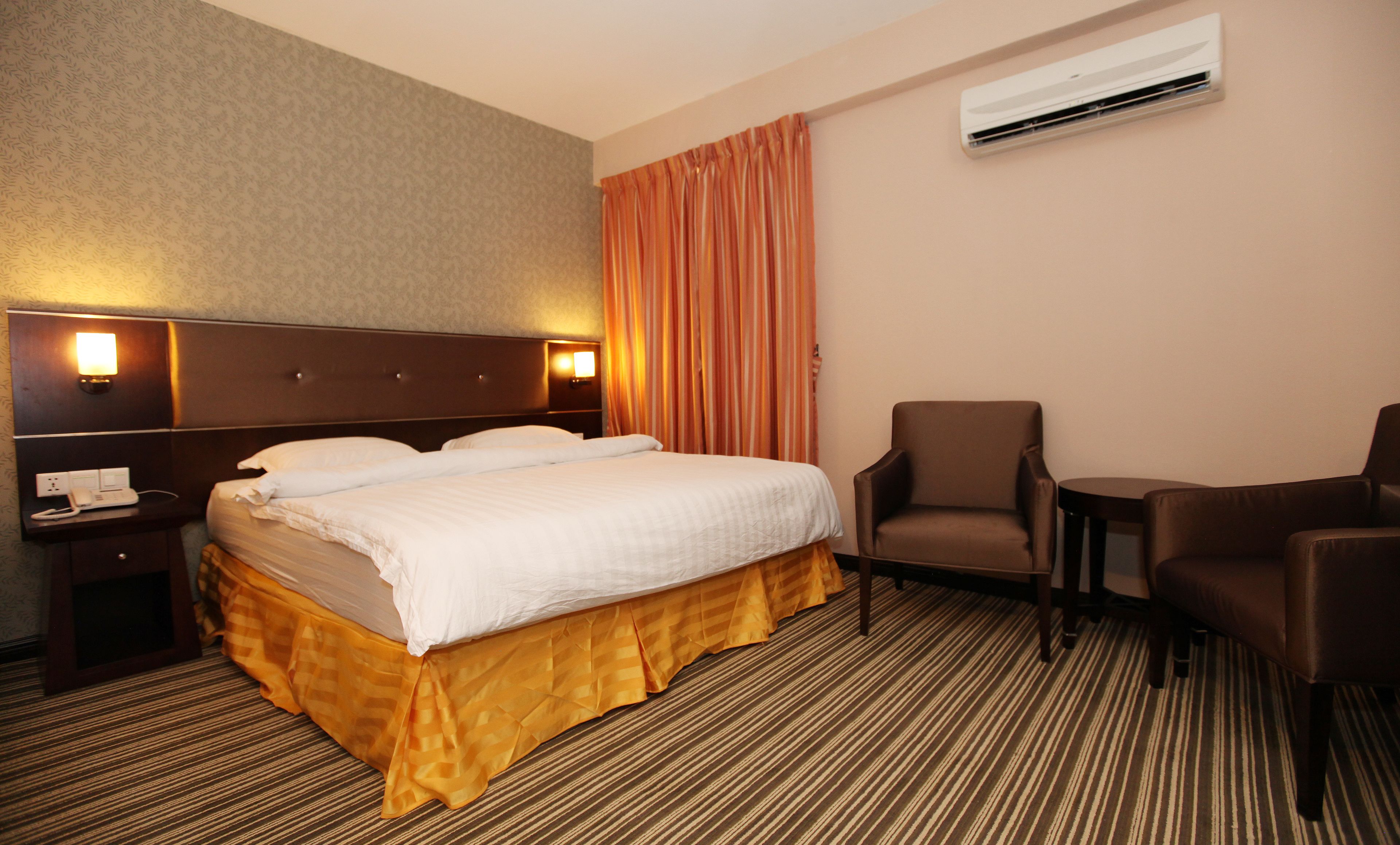 Una habitación de hotel con una cama grande, una silla, un escritorio y un equipo de aire acondicionado.