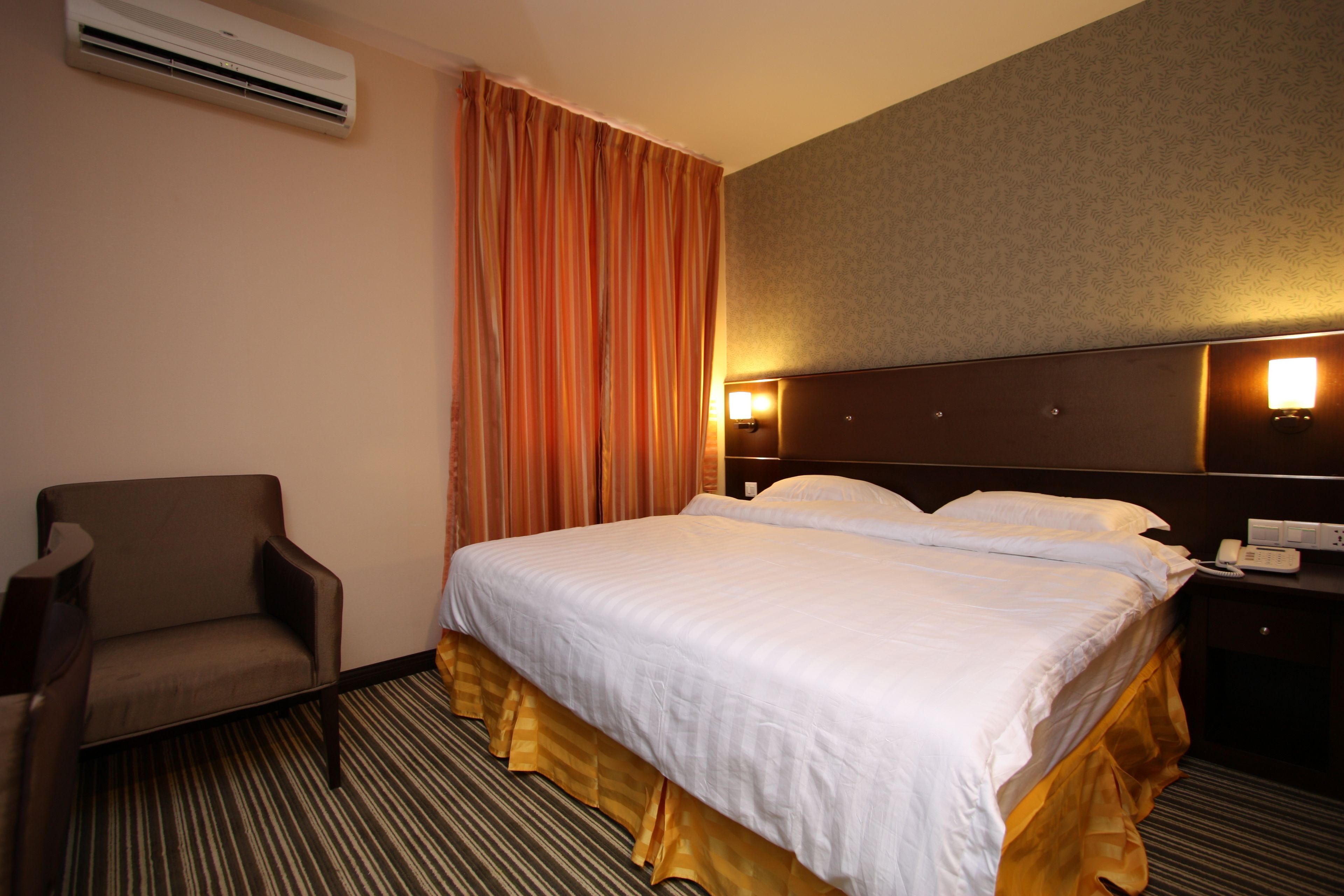 Ein Hotelzimmer mit Bett, Stuhl, Nachttisch und einer wandmontierten Klimaanlage.