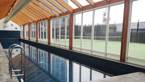 En inomhuspool med väggar av genomskinligt glas och ett tak av trä.