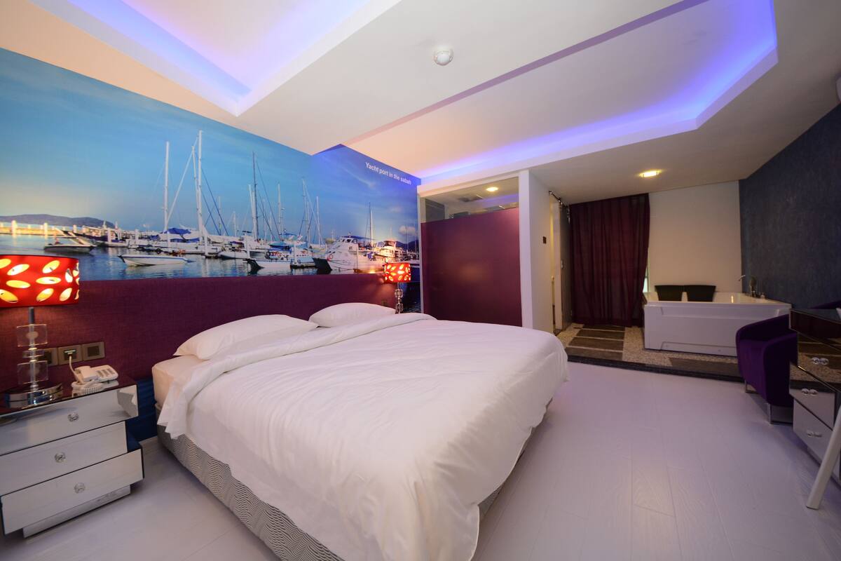 Habitación de hotel moderna con una cama grande, un escritorio, una silla, un baño y un mural que representa un puerto deportivo.