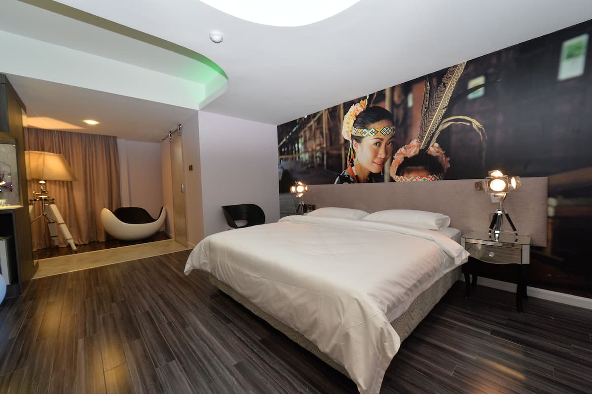 Una habitación de hotel moderna con una cama grande, un techo curvo, una zona de estar con una silla y un cuadro grande en la pared.