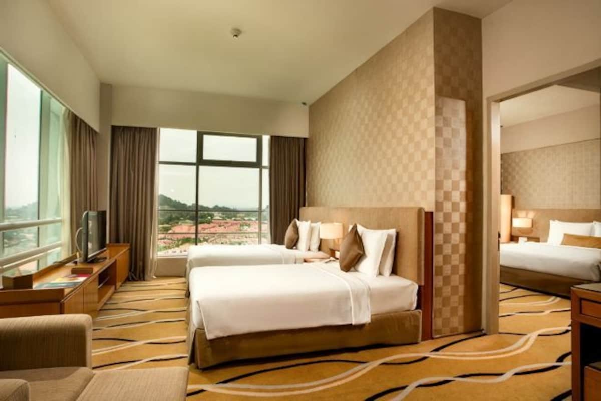 Quarto de hotel com duas camas, televisão, escrivaninha e uma janela grande com vista.