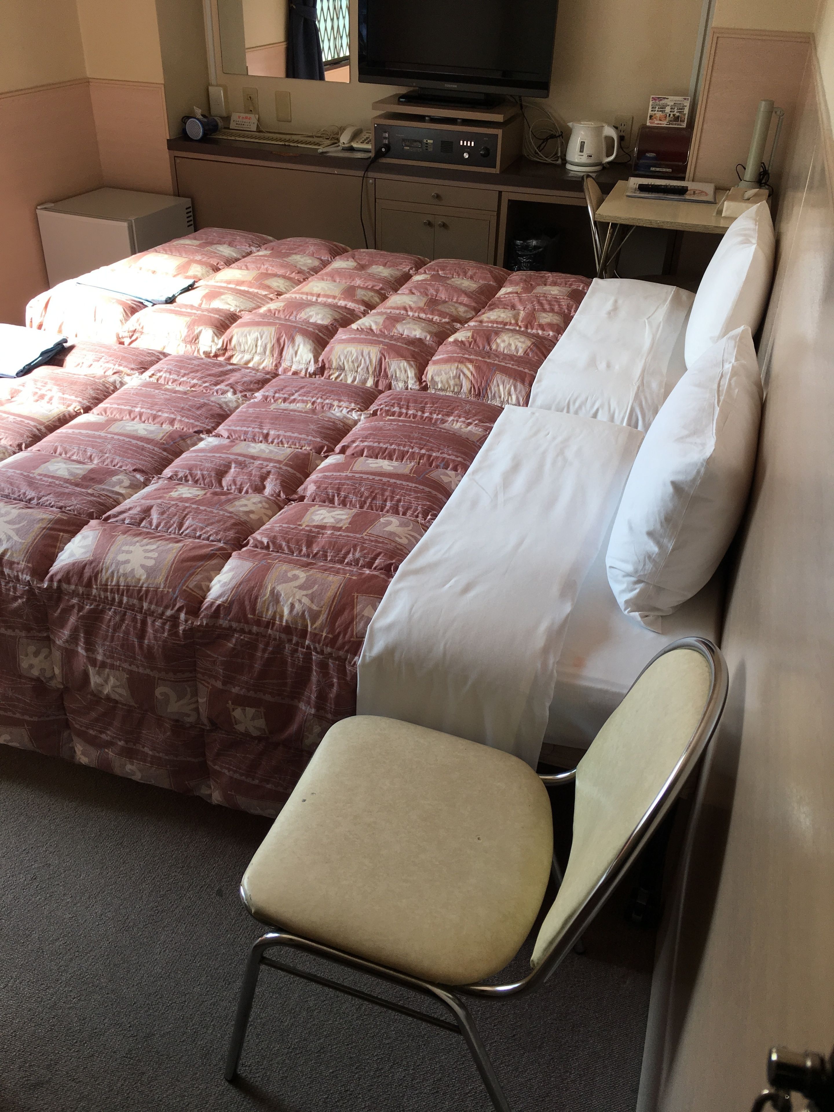 A hotel room with a bed, a chair, a desk with a computer, and a television.