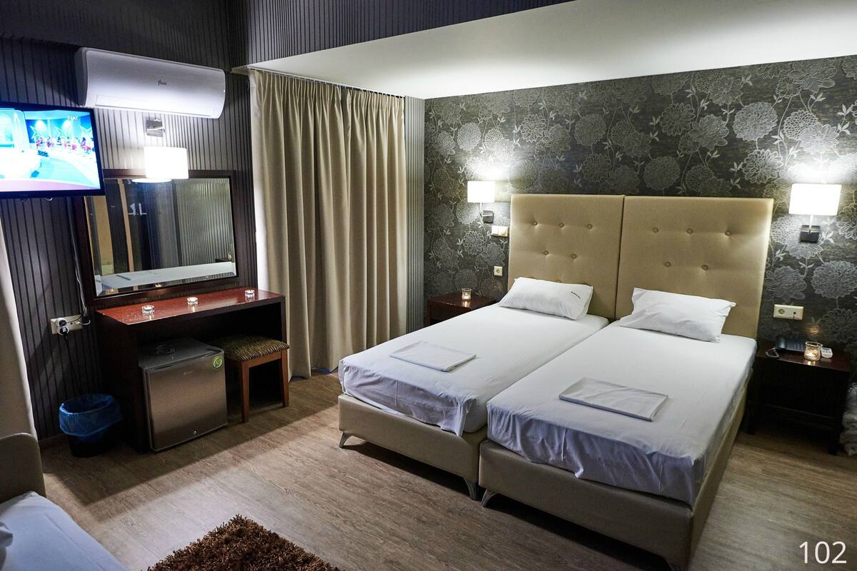 A hotel room with two beds, a TV, a desk with a computer, and a minibar.