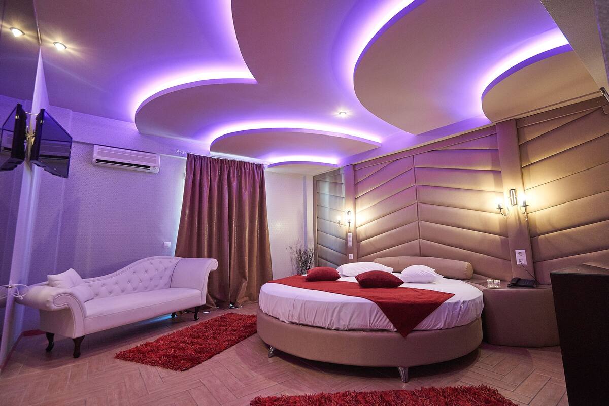 A modern bedroom with a curved ceiling, a round bed, a white sofa, and a red rug.