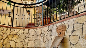 A stone wall with a decorative head sculpture, a metal staircase with a handrail, and a sign indicating an emergency exit. - Hotel Soleado (Taormina)