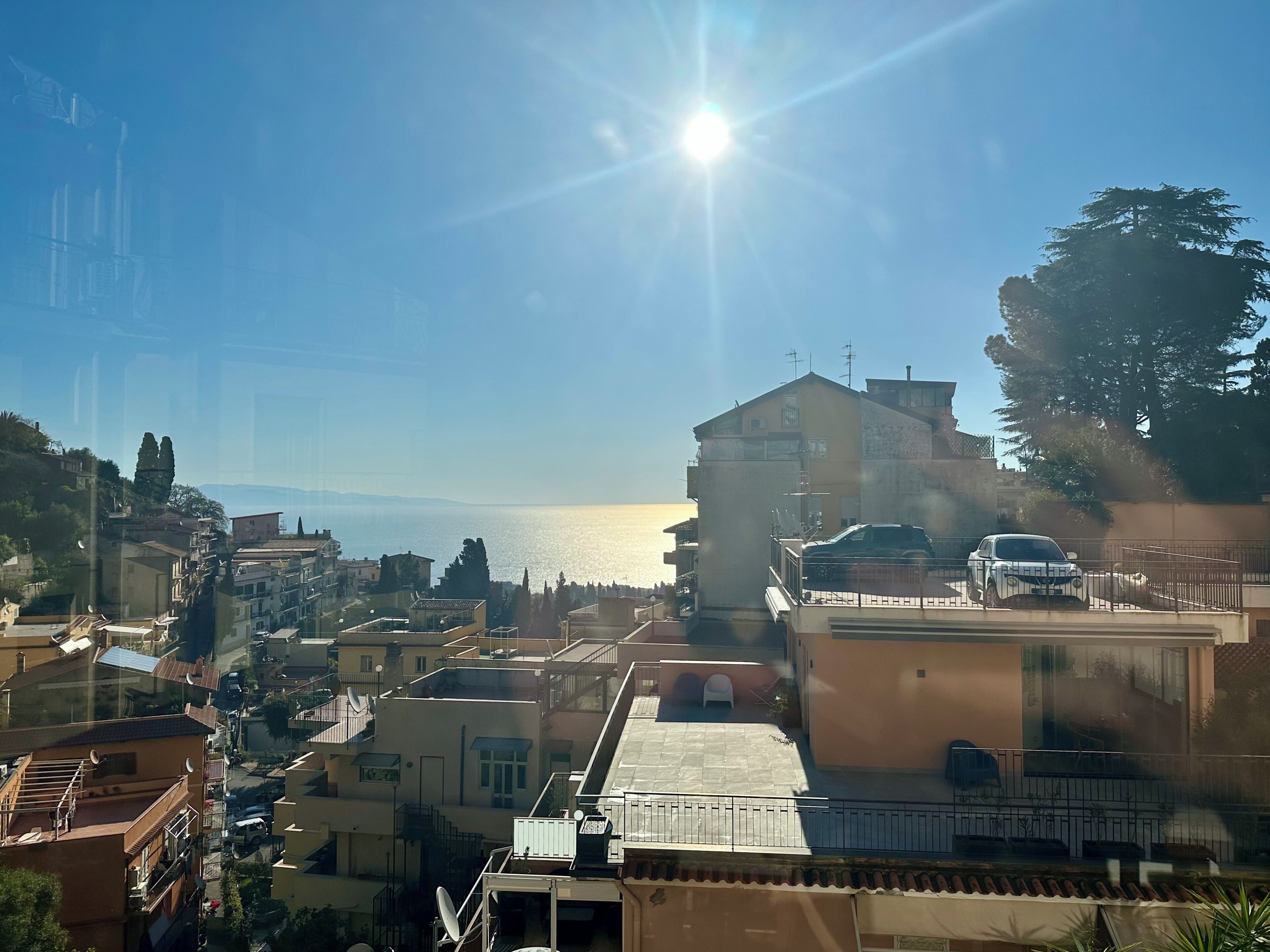 A residential area with buildings, a clear sky, and a view of the sea.