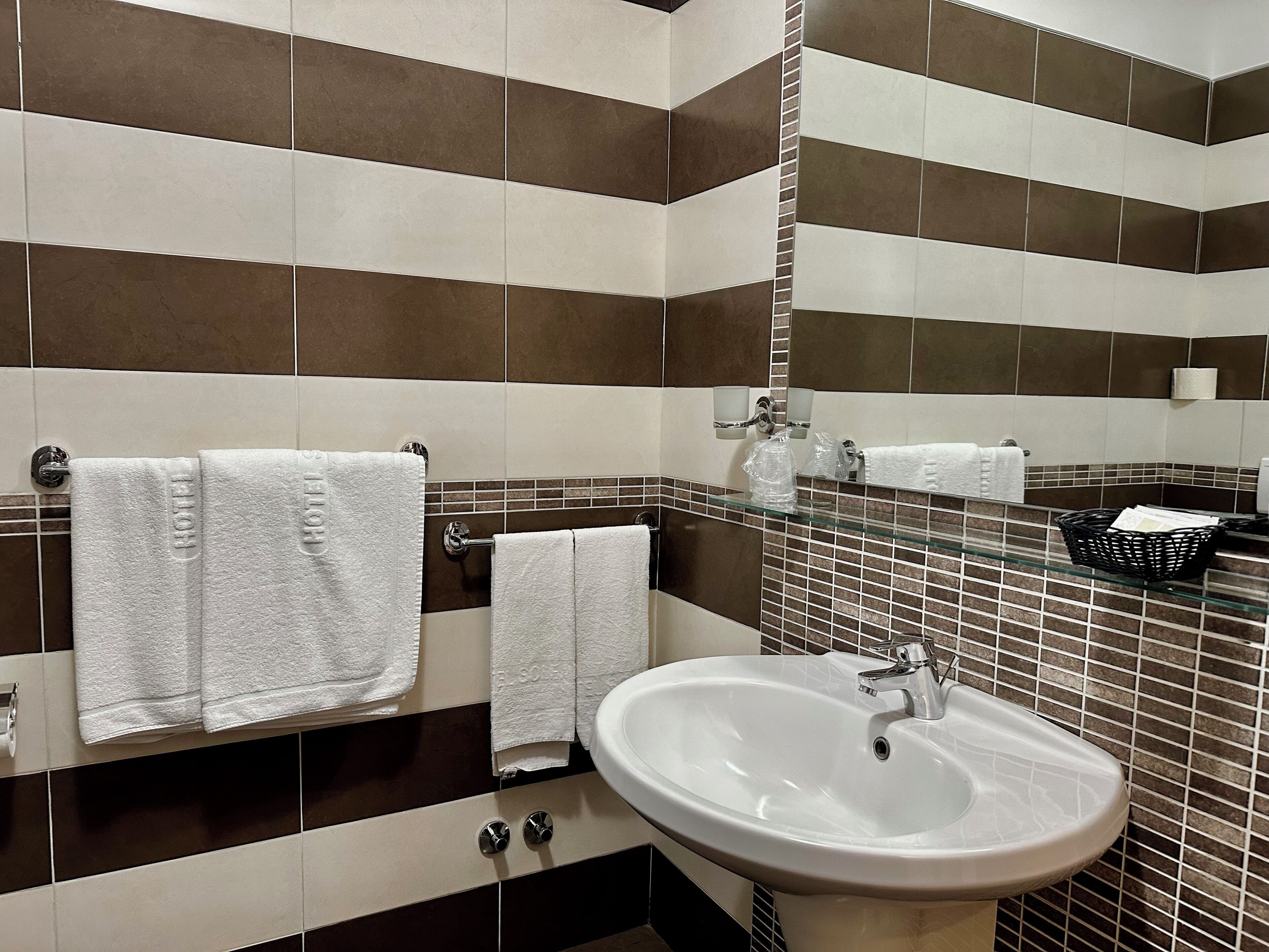 A bathroom with striped tile walls, a white sink, and two towels hanging on a rack.
