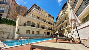 A swimming pool with lounge chairs and a stone wall. - Hotel Soleado (Taormina)