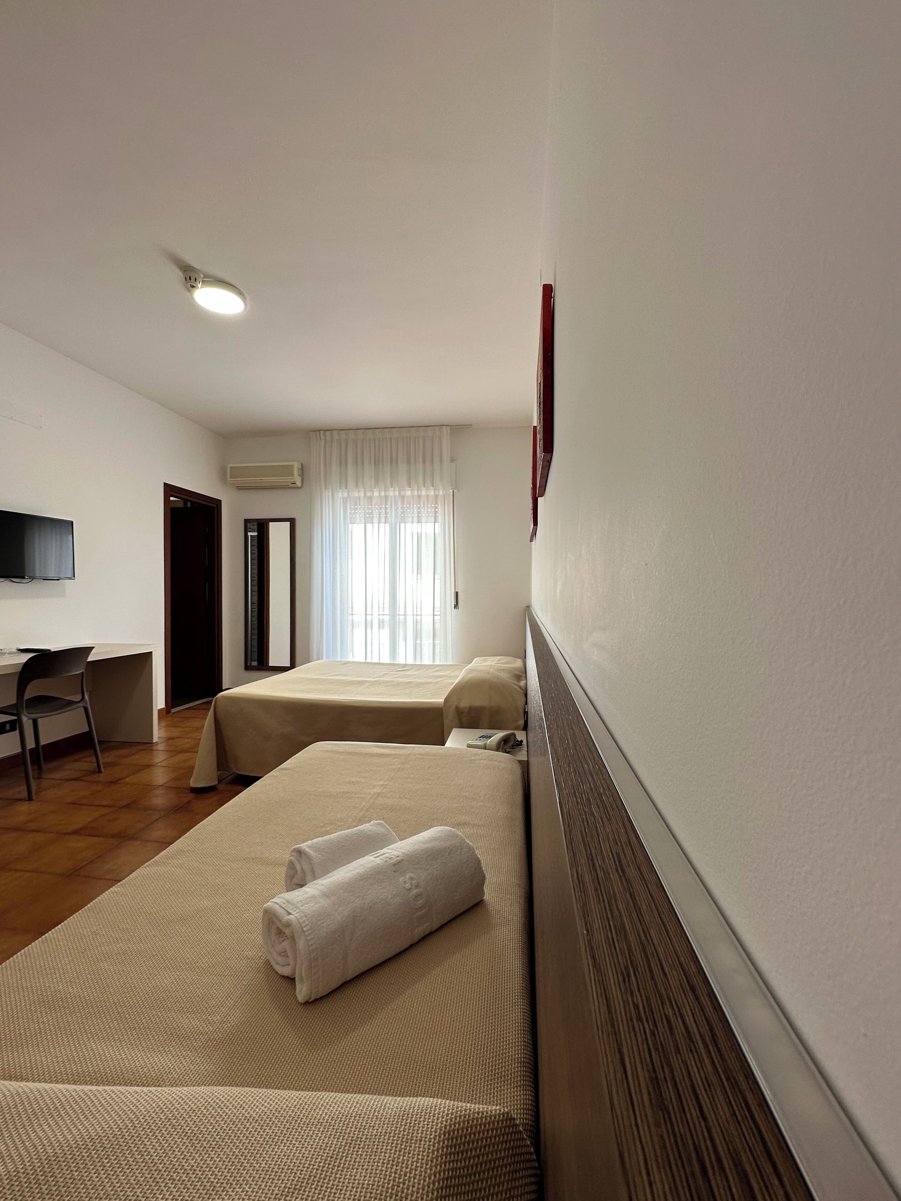 Une chambre d’hôtel avec deux lits, un bureau, une chaise, une télévision et un appareil de climatisation.