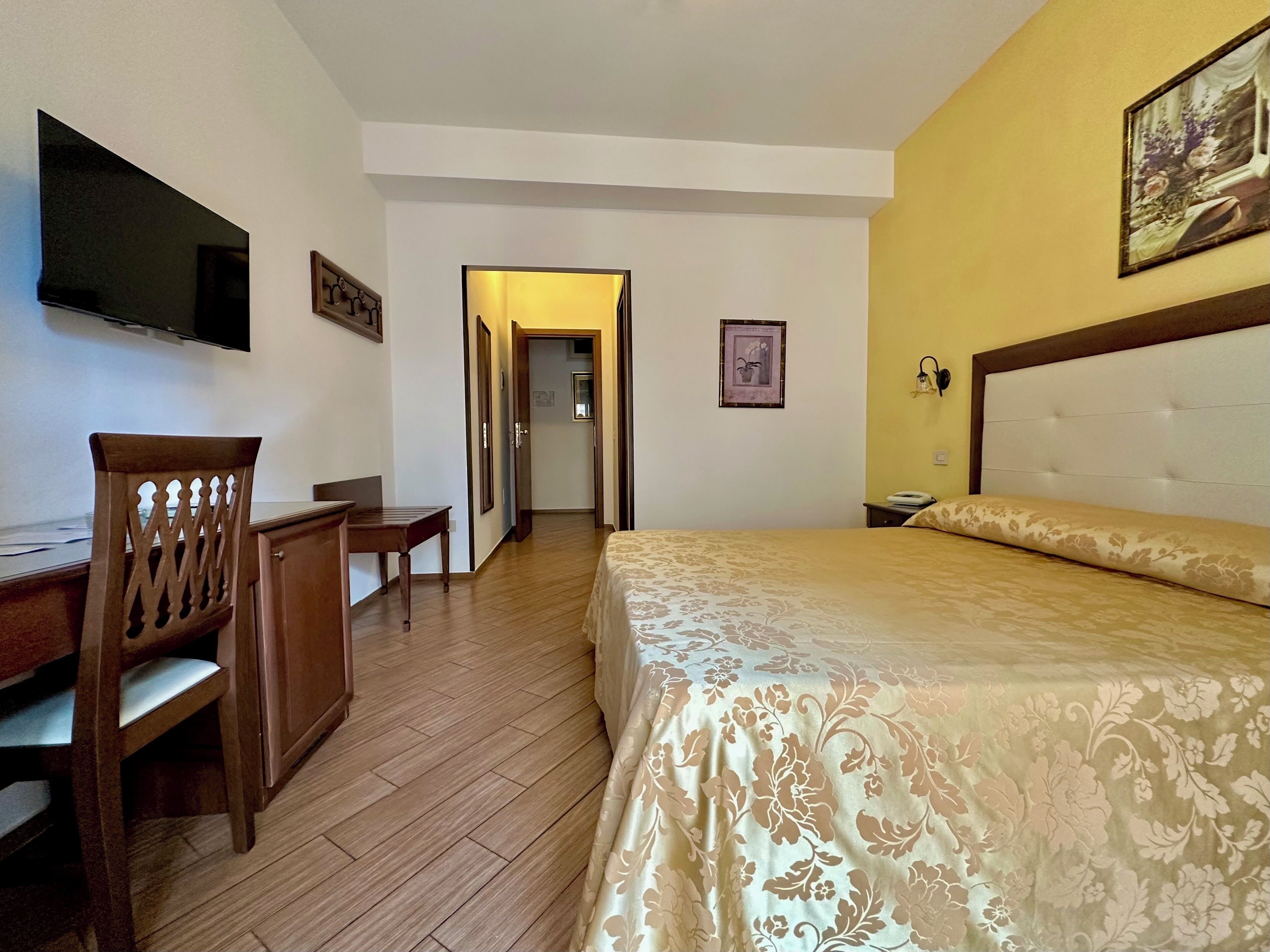 Habitación de hotel con cama, escritorio, silla, televisión y puerta que da a otra habitación.