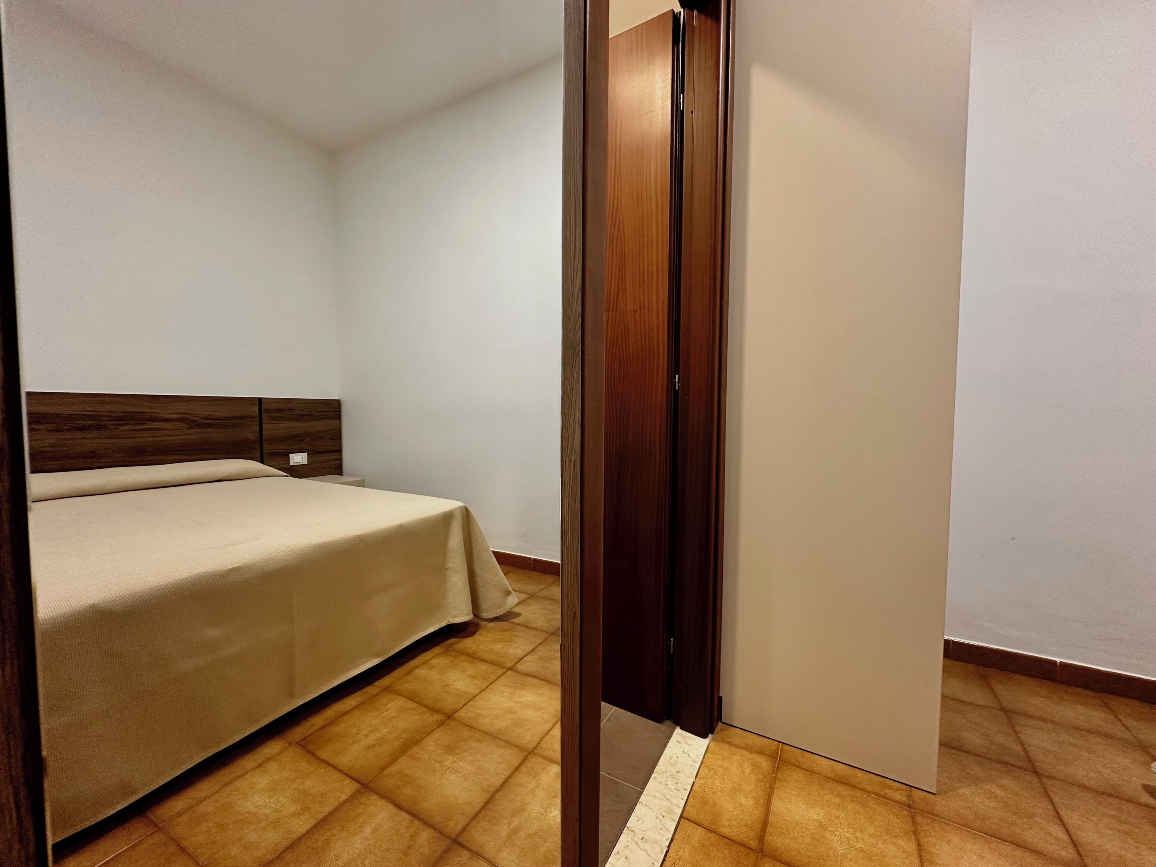 Ein Schlafzimmer mit einem Bett, einem Holzkopfteil, einem Kleiderschrank und einem Fliesenboden.